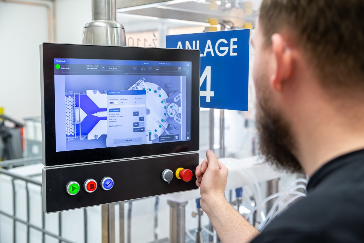 eine Person bedient ein Bedienfeld mit Touchscreen und Tasten einer industriellen automatisierten Abf&uuml;llanlage